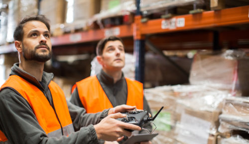 Two warehouse workers stocktaking warehouse inventory with drone, shipping and delivery logistic trends