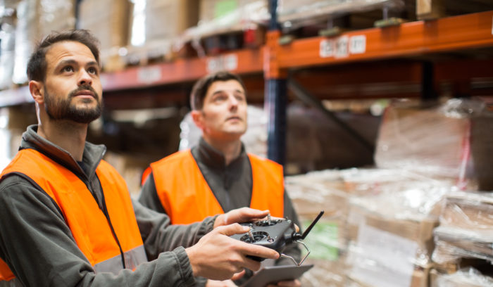 Two warehouse workers stocktaking warehouse inventory with drone, shipping and delivery logistic trends