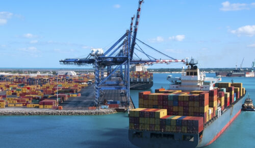 Port of Freeport Bahamas Container shipyard with heavy lifting Cranes and a ship coming in to dock assisted by tug boats